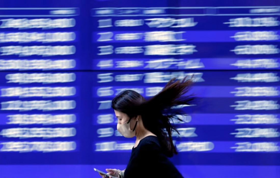 Một người qua đường đi ngang qua màn hình điện hiển thị những biến động gần đây của nhiều loại giá cổ phiếu khác nhau bên ngoài một ngân hàng ở Tokyo, Nhật Bản, ngày 22 tháng 3 năm 2023. REUTERS/Issei Kato
