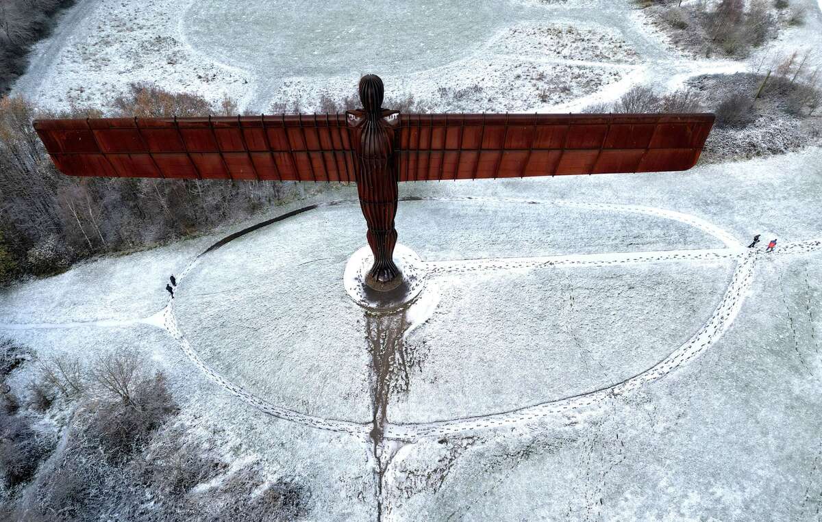 Người dân đi cạnh Thiên thần phương Bắc của Antony Gormley khi tuyết rơi ở Gateshead, Anh, ngày 30/11. (Ảnh: Reuters)